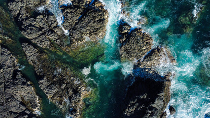 Drone top view of rock and dead coral formation with waves crashing on them 