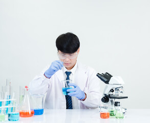 Fototapeta premium Asian male student scientist Wearing a doctor's gown in the lab looking hand at chemist. caused by mixing reagents in scientific research laboratories with test tubes and microscope on the table