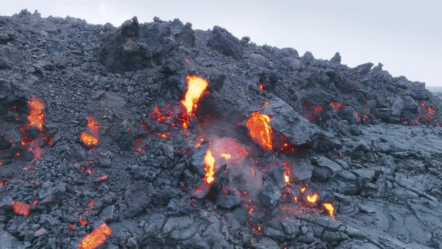 Flowing lava and black rocks. Red hot molten lava flowing from crater through streams on slope. Aerial lava flow on Big Island in Hawaii, USA shot on drone. Volcano eruption on Mauna Loa mountain