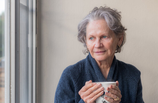 Closeup of senior woman holding tea cup and looking towards window (selective focus)