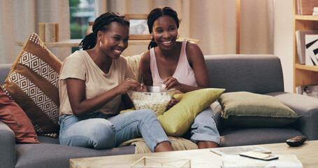 Movie night, happy and women with popcorn on the sofa for a television show, film or comedy. Smile, relax and African friends on the couch eating food and streaming a subscription service on tv