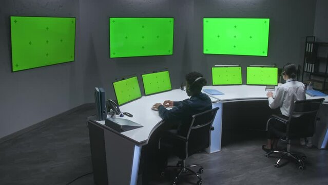 Multiracial male and female officers control CCTV cameras, work in security control center. Big digital screens and computer monitors with green screen, showing surveillance cameras video footage.