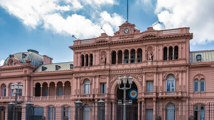 Fototapeta na wymiar The old pink house - Casa Rosada in Buenos Aires. A building with arches, galleries, columns, sculptures on the facade. Perimeter fence. Blue sky, clouds. Argentina.