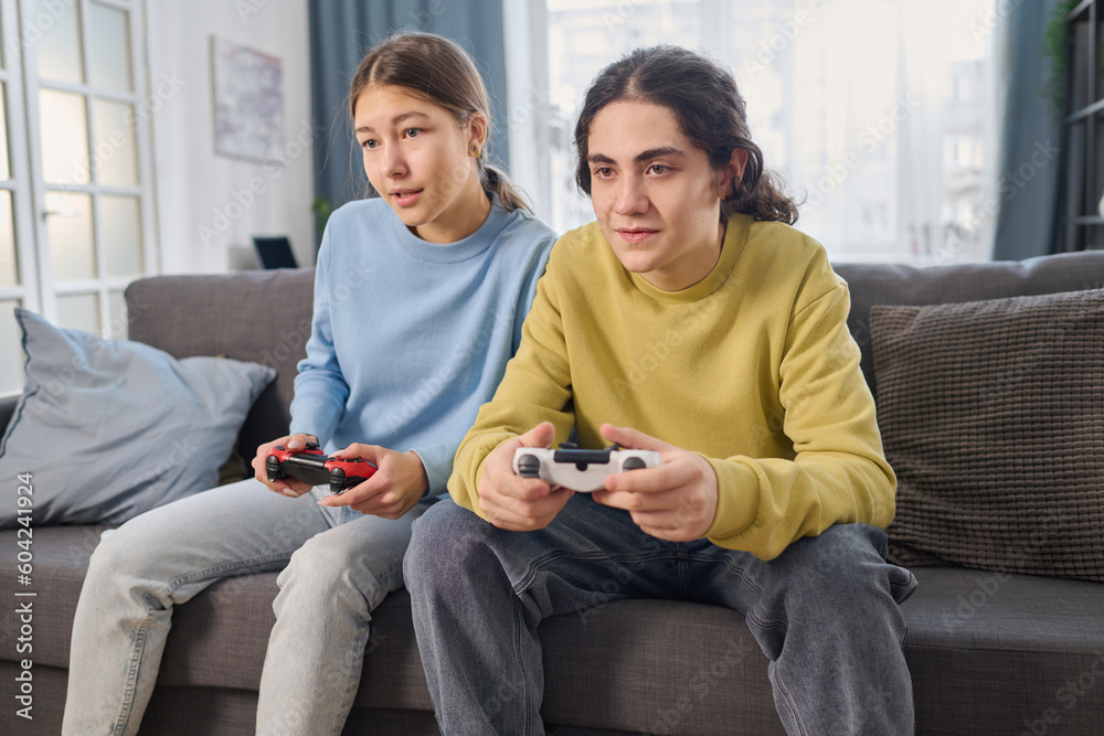 Wall mural Sibling sitting on sofa and playing game console together in the living room