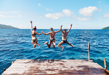 Water, back of people jumping off a pier holding hands and into the ocean together in blue sky....