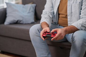 Close-up of mature man using joystick to play video game while sitting on sofa in the room