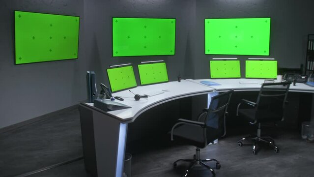 Workspace in security monitoring center for watching CCTV cameras. Computer monitors on the table and big digital screens on the wall with chromakey showing surveillance cameras footage. Green screen.