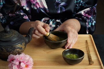 Woman tea master in kimono performs tea ceremony. Matcha green tea powder with a bamboo whisk and...