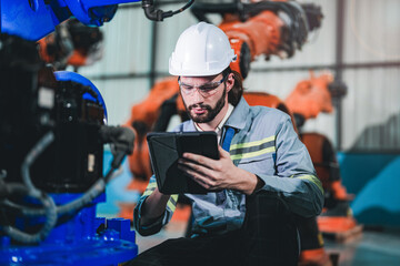 Factory engineer inspecting on machine with smart tablet. Worker works at heavy machine robot arm. The welding machine with a remote system in an industrial factory. Artificial intelligence concept. - obrazy, fototapety, plakaty