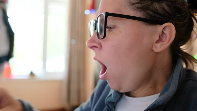 Close-up of the face of tired  girl who yawns while working at computer that is reflected in her glasses. Freelancer girl in office at home difficulty maintaining concentration and productivity while 