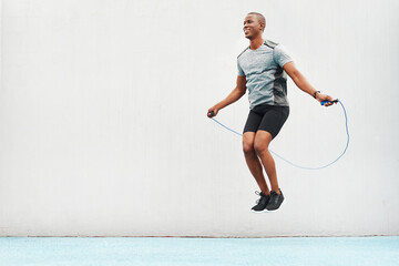 Jump, rope and space with black man skipping in stadium for sports, workout and cardio. Performance, health and body with male athlete training on track for strong, mockup and exercise by wall - obrazy, fototapety, plakaty