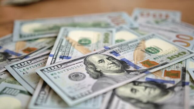 Slow motion close-up 100 American dollars bills. Many hundreds dollar paper money cash lies on wooden table. Idea financial success. 
