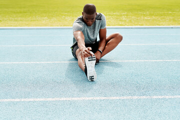 Athlete man, sitting and track for stretching legs to start training, exercise or running for fitness outdoor. African runner, warm up muscle or body for workout at stadium for race, contest or sport