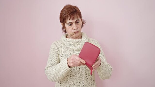 Mature hispanic woman looking at empty wallet over isolated pink background