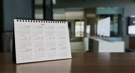 White calendar on brown wooden table in office.