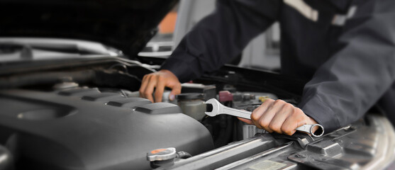 The mechanic works on the engine of the car in the garage, car repair service.	