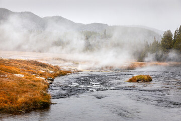 Boilng flowing water from geyser basin with white smoke in Yellowstone.