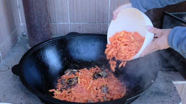 Cooking lamb pilaf in street kitchen. Female hands put the ingredients in cauldron. Outdoor cooking. Mouth-watering video where traditional pilaf dish is cooked.