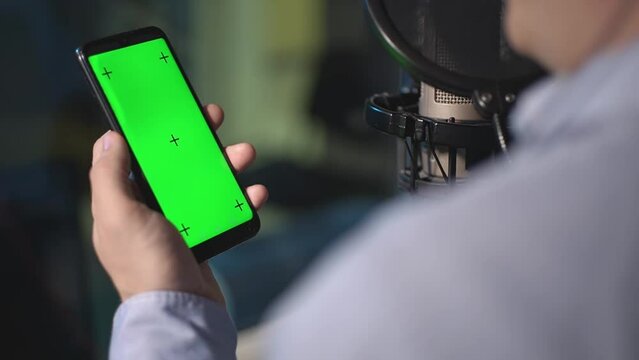 a man holds a phone with a green screen in his hands. he's in the recording studio. real time video. smartphone with green screen. close-up. High-quality FullHD video recording