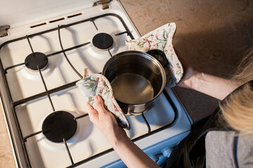 The girl puts a metal pan on a white gas stove in the kitchen. Image for your creative decoration or design.