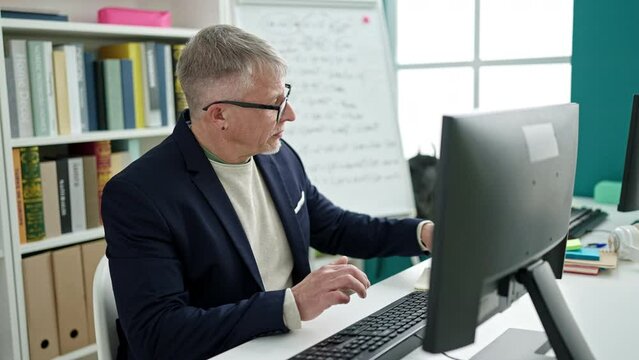 Middle age grey-haired man teacher using computer studying at university classroom