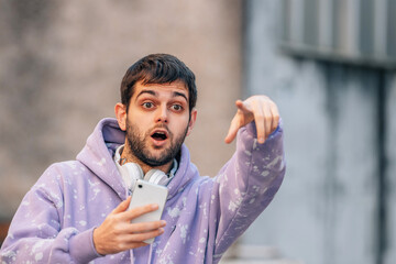 young man in the street pointing surprised with phone