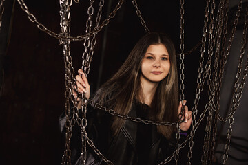 Lovely stylish teen girl 13-14 year in retro style image posing in dark industry room with chains, looking at camera. Pretty teenage girl model actress. Fashionable style concept. Copy ad text space