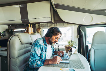 One man using computer and phone sitting indoor inside camper van modern vehicle. People enjoying technology and connection in travel vacation lifestyle. Living vanlife and working. New job office