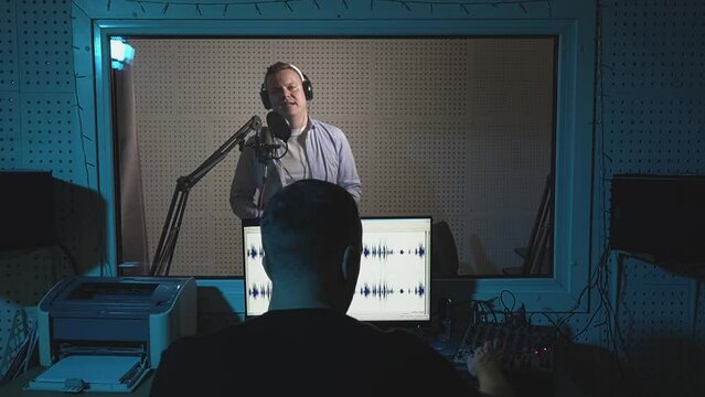 a man in headphones speaks into a microphone in a recording studio. A sound engineer records a person's voice in a sound recording studio. slow motion video. High quality Full HD video recording