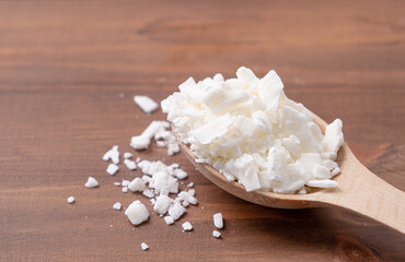 soy wax in wooden spoon on wooden background, copy space