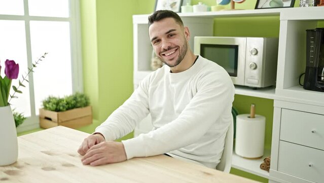 Young hispanic man smiling confident sitting on table at dinning room
