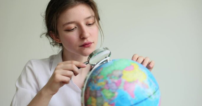 Tourist woman looks through magnifying glass at globe. Girl going abroad to go for weekend and air travel concept