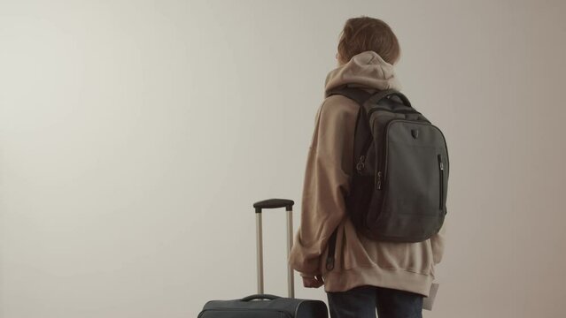 Young adult woman with a backpack, a suitcase and paper documents on a white background. Back view. Foreign student. Refugee or immigrant