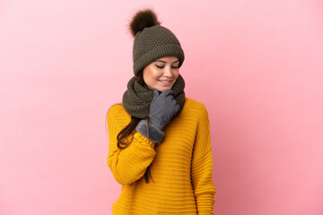 Young caucasian girl with winter hat isolated on pink background looking to the side and smiling