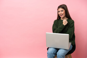 Young caucasian woman sitting on a chair with her laptop isolated on pink background celebrating a victory