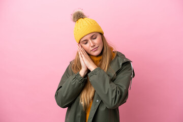 Young blonde woman wearing winter jacket isolated on pink background making sleep gesture in dorable expression