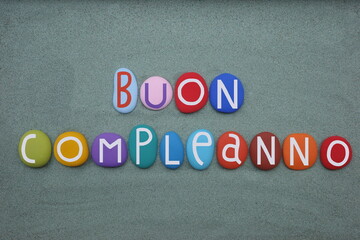 Buon compleanno, italian Happy Birthday text composed with multi colored stone letters over green...