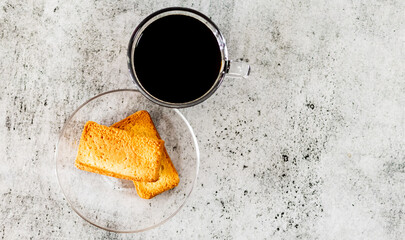 Black coffee with rusk in saucer placed on a textured surface.