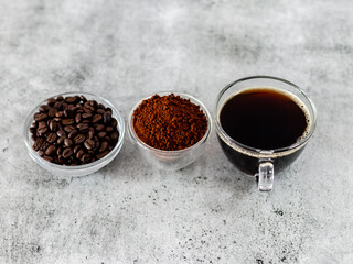 Close shot of coffee beans, ground coffee and cup of black coffee over white background.