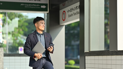 Fototapeta premium Businessman in full suit using smartphone in subway station during his morning commute