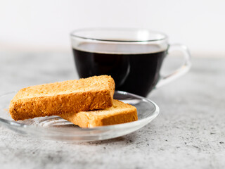 Closeup shot of rusk in saucer with defoused black coffee on background.