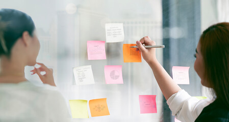 Businesswoman meeting at office and use sticky notes on glass wall in office,  planning work together brainstorm strategy.
