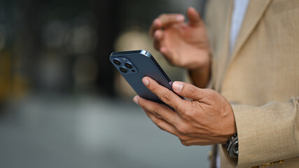 Select focus on hand of businessman using smartphone while standing outdoor. Technology, business and communicating