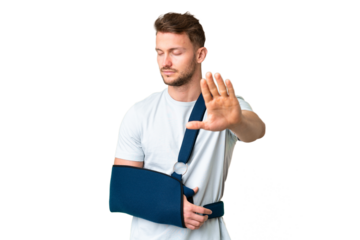 Young caucasian man with broken arm and wearing a sling over isolated chroma key background making stop gesture and disappointed