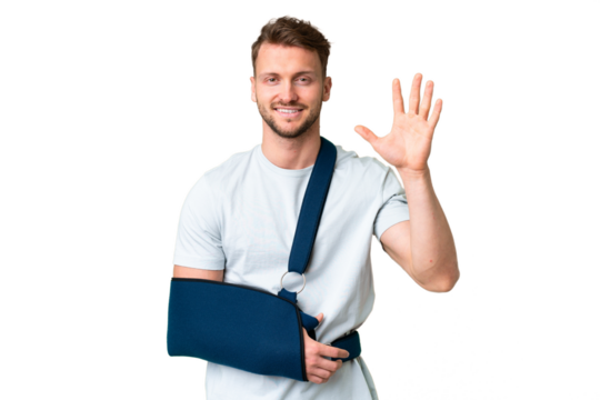 Young caucasian man with broken arm and wearing a sling over isolated chroma key background saluting with hand with happy expression