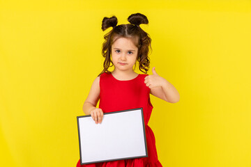 little brunette girl in red drees smiling and holding an empty drawing Board, space for text,isolate on a yellow background