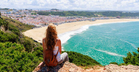 woman tourist sitting on cliff and enjoying panoramic view of atlantic ocean, Nazare beach in...
