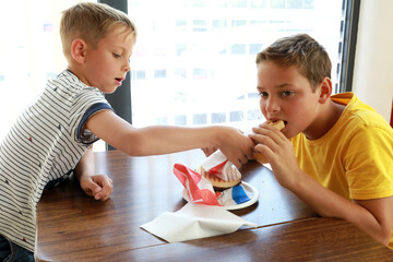 Child giving his brother try hot dog