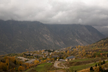 Panoramic view of a mountain landscape, large meadows of fresh green grass crossed by a winding, curving road leading to a small village of stone houses with slate roofs in Cerler, Huesca, Aragon.