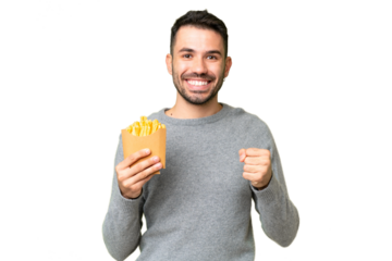 Young caucasian man holding fried chips over isolated chroma key background celebrating a victory in winner position